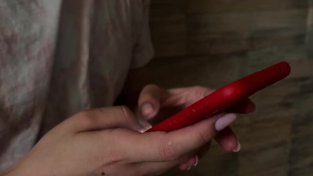 Woman's hands using a red smartphone, scrolling through a social media feed and texting a message in a dark room while relaxing at home in the evening