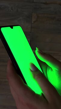 Woman's hand scrolling and swiping up on a smartphone with a green screen at night, illustrating modern communication, digital interface use, and network browsing