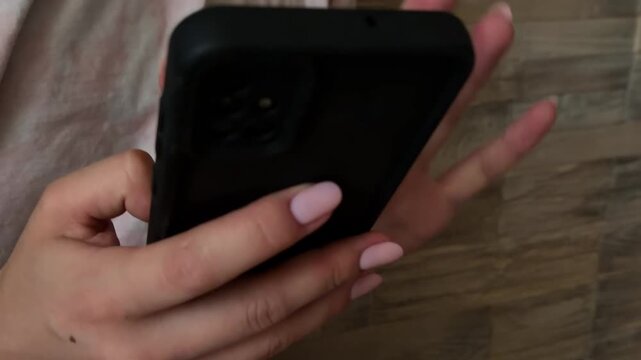 Woman's hands with pink manicure scrolling through social media feed on a smartphone. Young female person using a modern cell phone for online communication and browsing