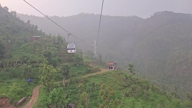 Scenic footage from the Manakamana cable car showing a passenger gondola traveling above densely forested mountain slopes, winding river valley, roads, settlements, and surrounding Himalayan foothills