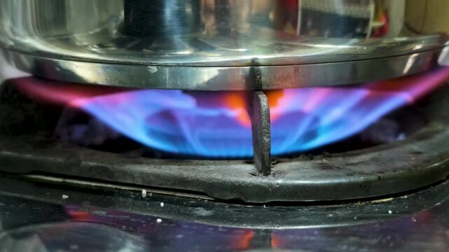 Close-up of blue gas flame burning under a stainless steel pot on a kitchen stove