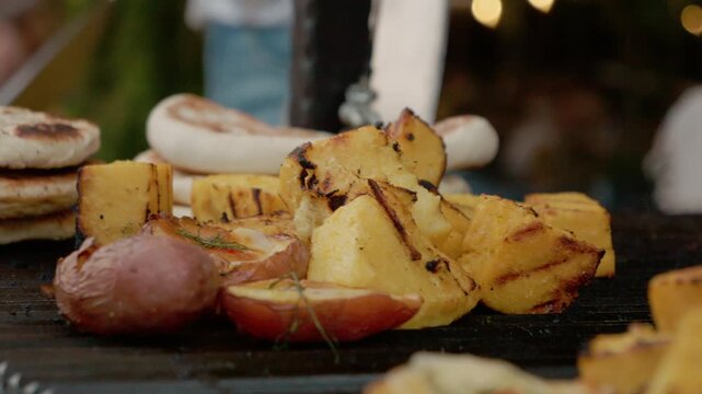 A whole baked potato is shown on a grill plate along with grilled vegetables at a street food festival. The event features various grill items for visitors.