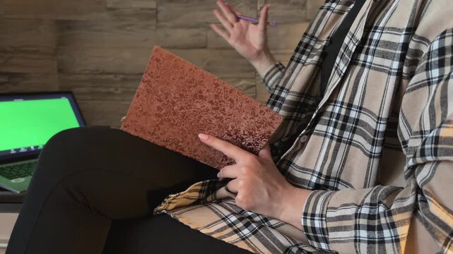Psychologist holding a notebook during an online therapy session with a green screen laptop, gesturing and providing mental health consultation to a patient via video call