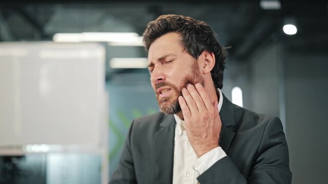 Professional at office desk develops sudden tooth pain. Expresses discomfort and severe dental ache, indicating need for relief. Workplace pain causing disruption.
