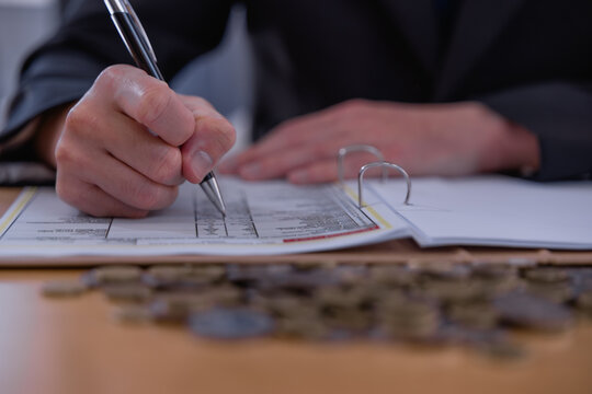 Business professional reviewing financial documents and writing accounting records with coins on desk, representing bookkeeping, budgeting, expense management, audit and financial planning.