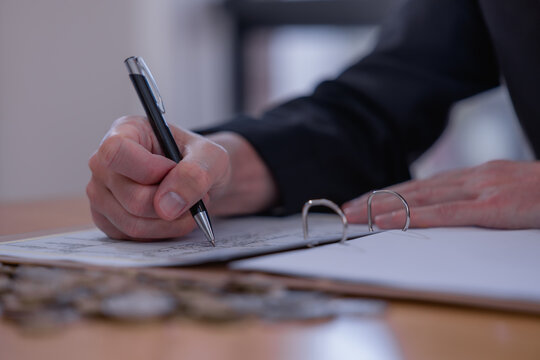 Business professional reviewing financial documents and writing accounting records with coins on desk, representing bookkeeping, budgeting, expense management, audit and financial planning.