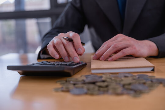 Business professional reviewing financial documents and writing accounting records with coins on desk, representing bookkeeping, budgeting, expense management, audit and financial planning.