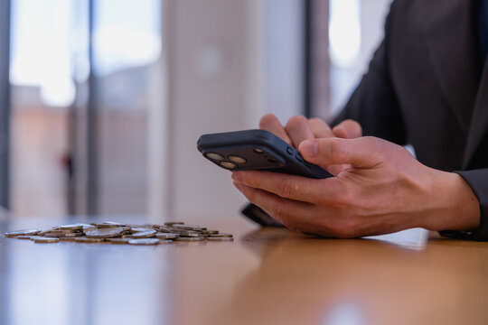 Business professional using smartphone with coins on desk, representing mobile banking, digital finance investment savings financial planning fintech technology and money management.