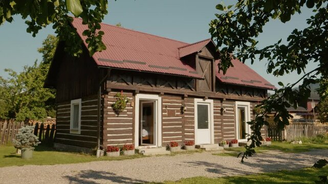 A traditional house in Bucovina. The home features wooden design elements and a simple garden. People can be seen walking around the area.