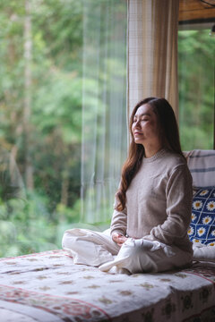 Vertical portrait image of a woman meditating on the bed at home