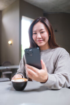 Vertical portrait image of a woman drinking coffee while using mobile phone in cafe