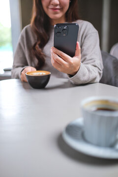 Vertical closeup image of a woman drinking coffee while using mobile phone in cafe