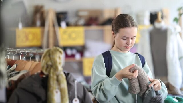 Positive adolescent female customer holding knitted hat for cold season in retail outlet