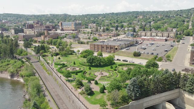 Aerial orbit view of Leif Erikson Park Rose Garden with circular flower beds beside Duluth downtown skyline