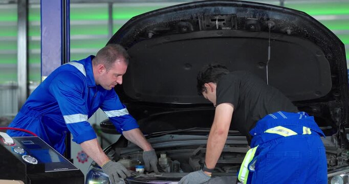  Auto mechanics servicing electric car air conditioning system with refrigerant recharge machine