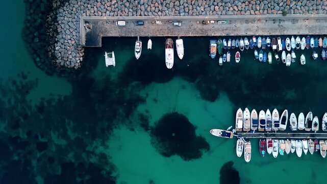 Aerial top down view of the picturesque fishing port, moored boats, and turquoise coastal waters of Sferracavallo in Palermo, Sicily, Italy