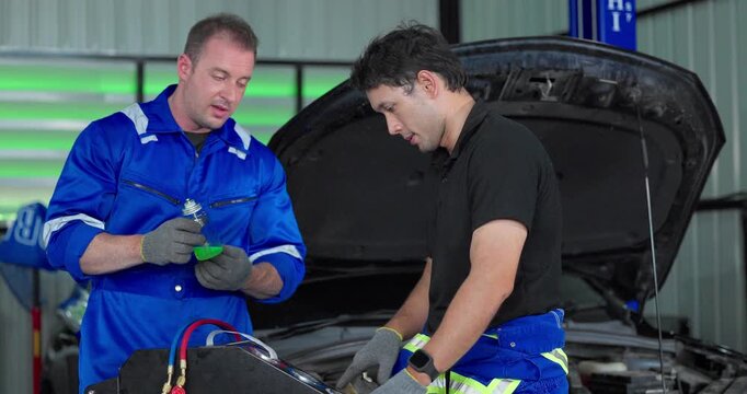 Auto mechanics servicing electric car air conditioning system with refrigerant recharge machine