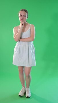 Teen girl dressed in light summer dress standing with thoughtful and sad-think look against green screen, chroma key compositing