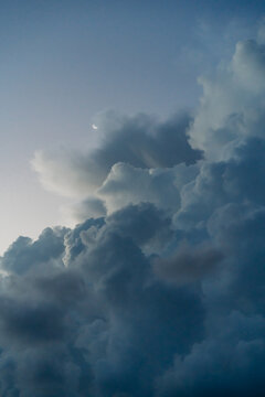 Crescent moon visible among dramatic moody clouds