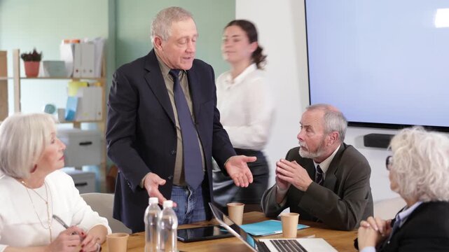  Mature male leader, trainer talking to group of people, brainstorming, discussing ideas in auditory