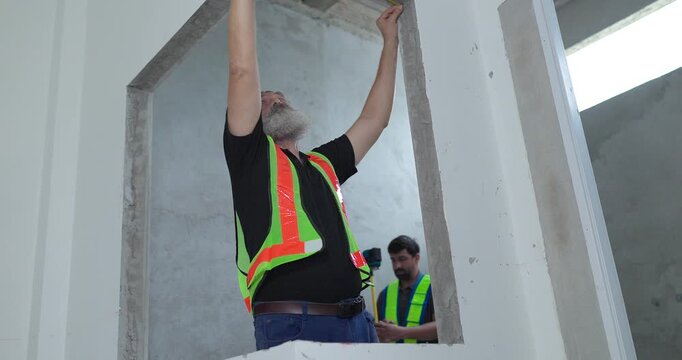 Construction worker measuring window opening with tape measure at house building site