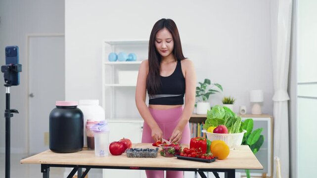 Wellness influencer talking about weight loss diet while filming in modern kitchen. Beautiful Asian woman producing engaging video content about natural healthy eating habits.