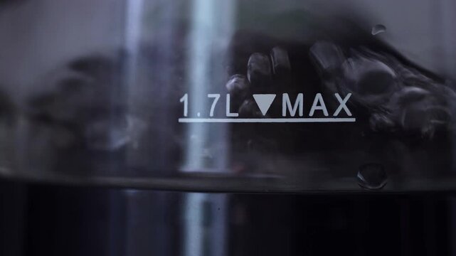 Close up water bubbling rapidly inside glass kettle near 1.7L MAX level mark line.