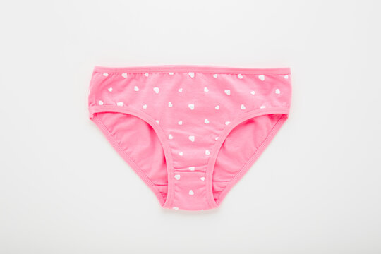 New pink panties with white heart shapes for little child girl on light gray table background. Closeup. Flat lay. Closeup. Top down view.