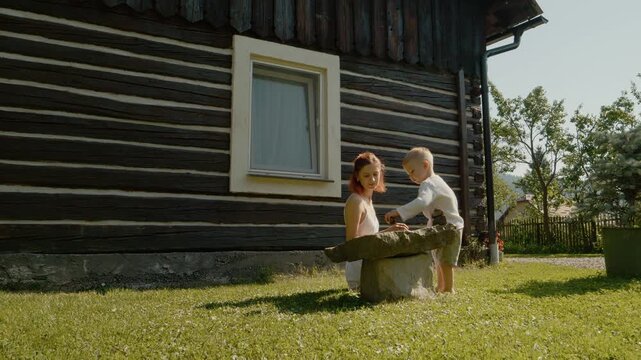 A woman and her little boy have fun playing together in front of a traditional house in Bucovina. They enjoy their time outdoors on a nice day.
