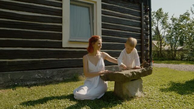 A woman and her little boy spend time outside a traditional house in Bucovina. She touches his cheek and admires him as they play in the grass.