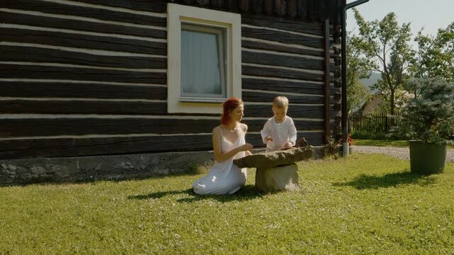 A woman and her little boy have fun with petrices in the grass. They are in front of a traditional house in Bucovina. They enjoy their time outdoors together.