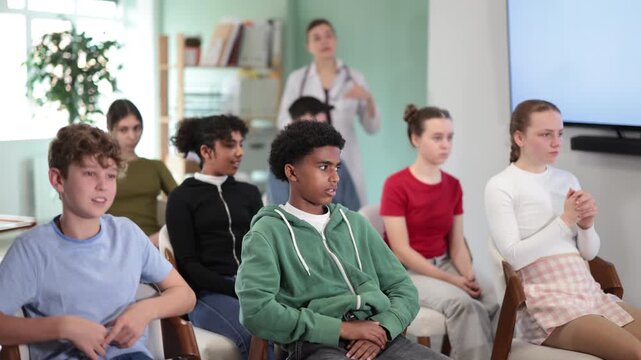 Schoolchildren, boys and girls, carefully watch a lecture in the classroom against the background of a a doctor teacher. Teenage children in a general education lesson . High quality 4k footage