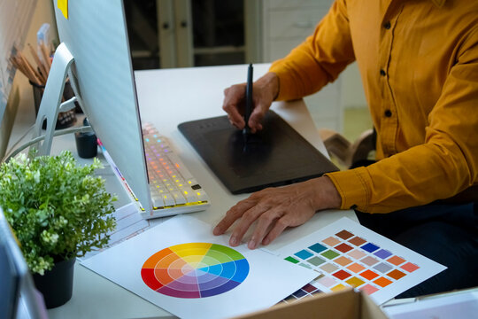 Graphic Designer Using Drawing Tablet with Color Wheel and Swatches on Creative Workspace Desk