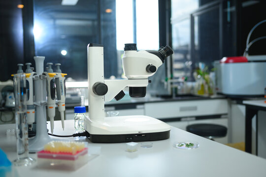 Stereo Microscope with Pipettes and Lab Equipment on White Workbench in Modern Scientific Laboratory
