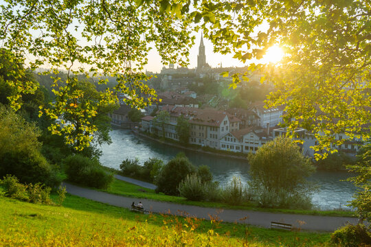 Vista panor&aacute;mica de Berna al atardecer sobre el r&iacute;o Aar rodeada de vegetaci&oacute;n exuberante y la catedral de la ciudad al fondo.
