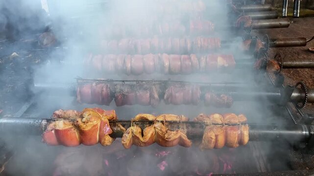 Traditional Pork Belly Roast Cooking on Rotisserie over Hot Coals with Smoke