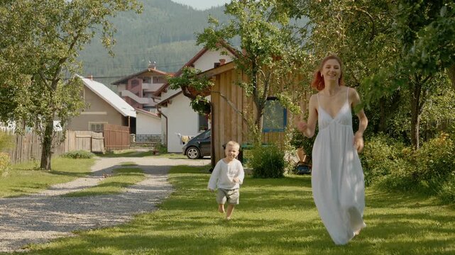 A woman and her little boy play and run together in the yard. They enjoy each others company in the fresh air. It is a happy day outside in the countryside.