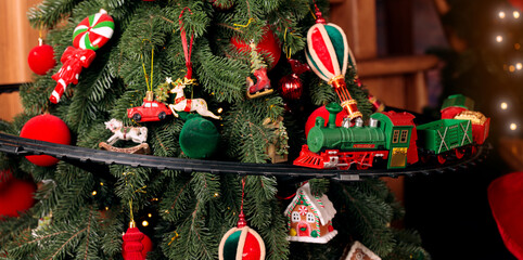 Festive Christmas tree adorned with red and green ornaments and a toy train © Artem Kniaz
