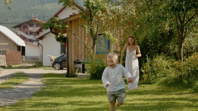 A woman and her little boy enjoy time in the yard. They run and play on the grass while the sun shines. Family fun happens outdoors on a warm day.