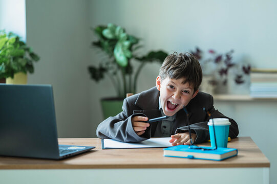 Excited boy plays a businessman at an office desk