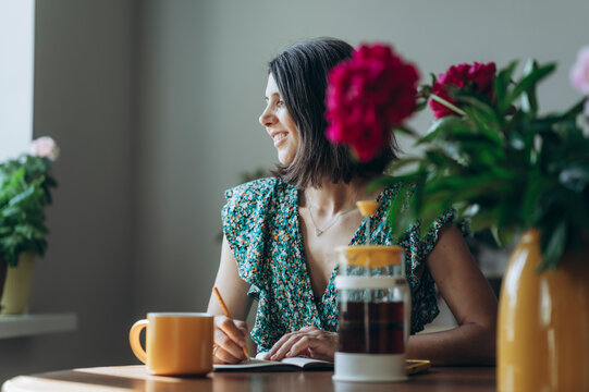 Smiling woman writing in diary at home while drinking morning tea