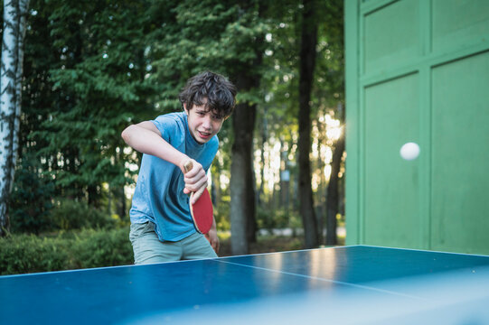 A teenage boy plays table tennis outdoors in the park