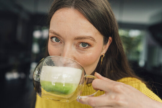A woman drinks a homemade matcha latte with a milk beard at home