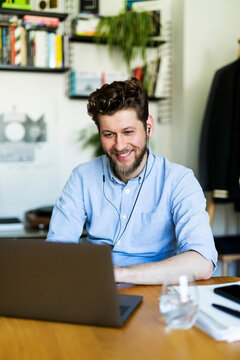 Smiling man joins a video call on a laptop in his home office