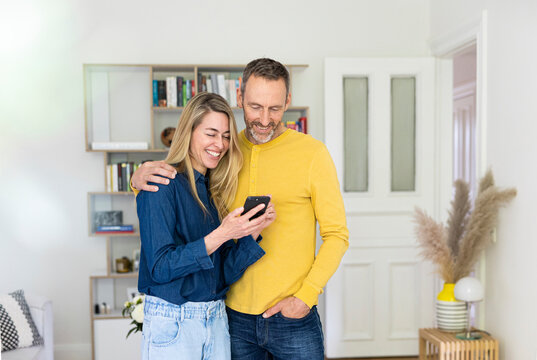 A smiling couple looks at a mobile phone in the living room
