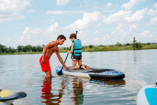 A coach teaches a child paddleboarding on a lake in summer