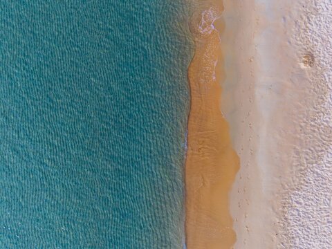 Turquoise sea water meets sandy beach in an aerial view