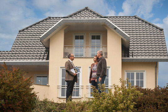 Estate agent communicating with potential buyers in front of residential house