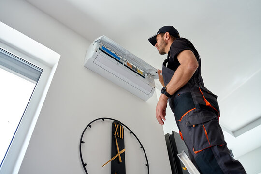 Air conditioner technician inspecting open wall mounted unit at home