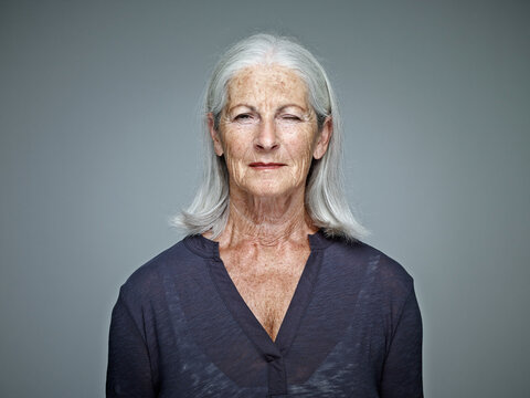 Portrait of senior woman with grey hair in front of grey background